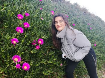 Portrait of beautiful young woman standing by pink flowering plants