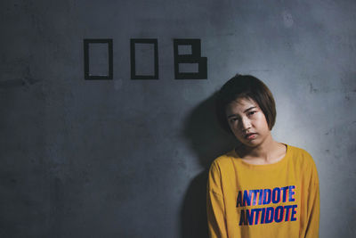 Portrait of young woman standing against wall