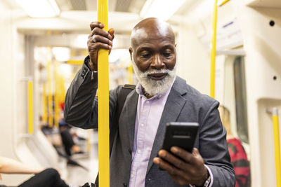 Senior commuter using mobile phone and holding pole in train