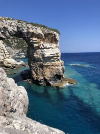 Built structure on rocks by sea against clear blue sky