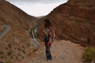 Woman looking away while standing on field against rocky mountains