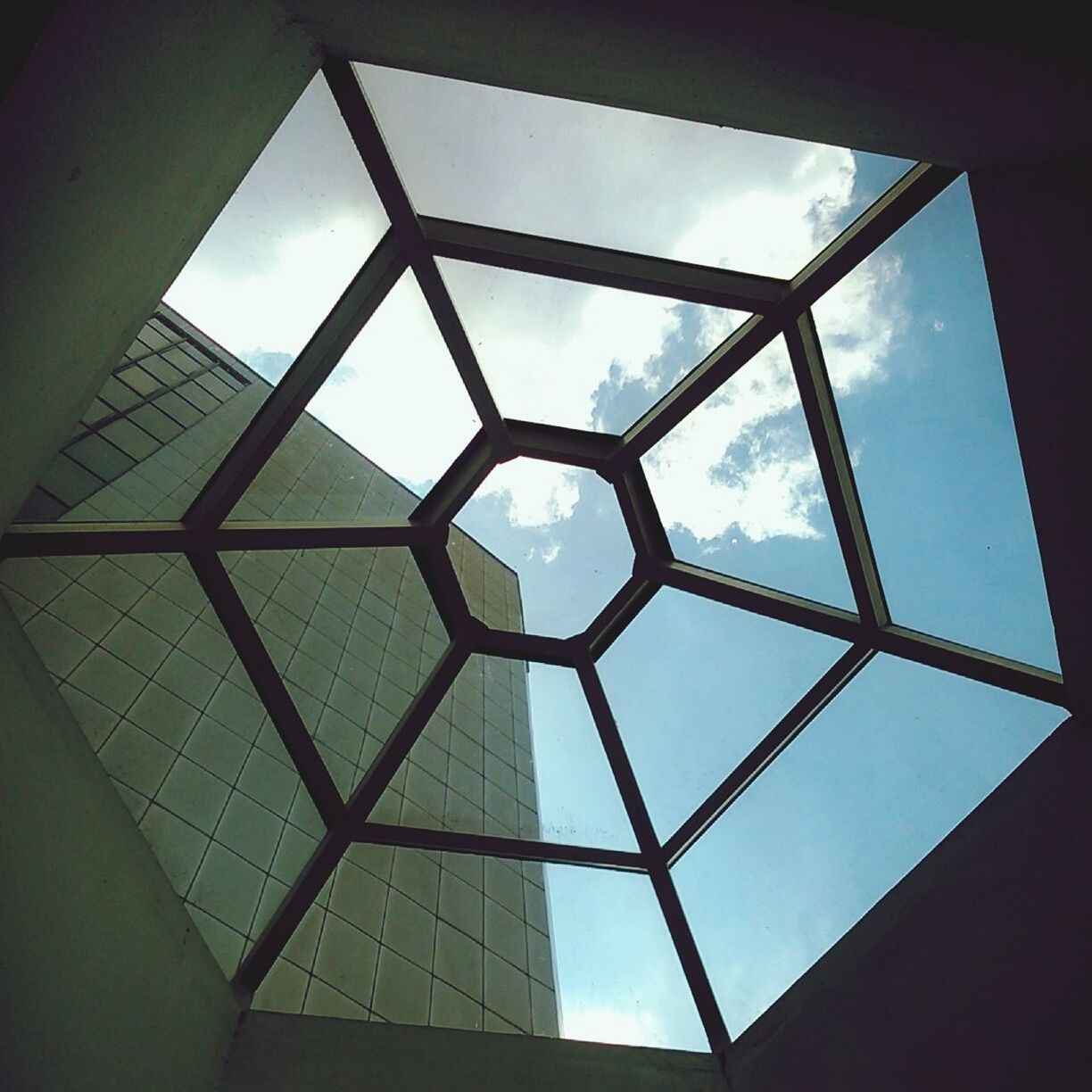 low angle view, architecture, built structure, sky, glass - material, window, indoors, directly below, geometric shape, building exterior, cloud - sky, transparent, skylight, cloud, day, building, modern, no people, pattern, glass