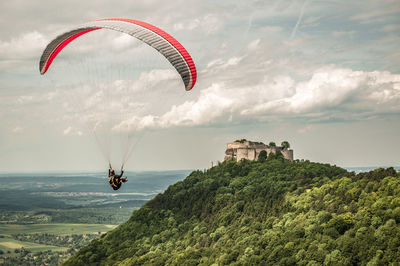 Person paragliding by swabian jura against cloudy sky