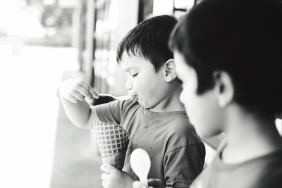 Boy eating ice cream cone with male friend standing outdoors