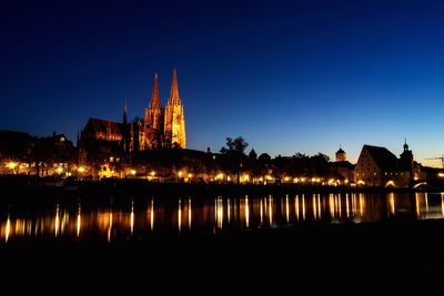 Illuminated buildings by river against sky at night