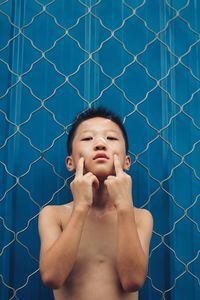 Portrait of shirtless man standing against fence