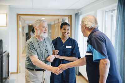 Senior man arm in arm with female nurse while giving friend handshake in alley at nursing home