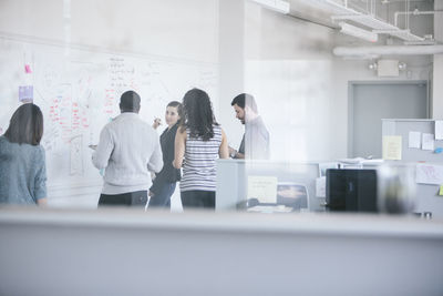 Businesswoman explaining to colleagues by whiteboard seen through glass