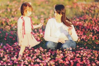 Cute girl standing by mother amidst pink flowers on land