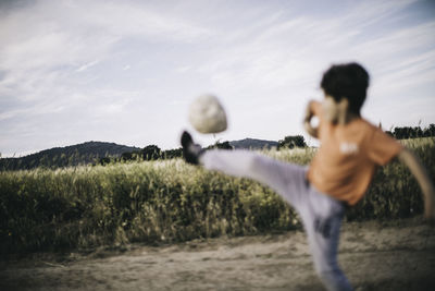 Boy playing with ball on field against sky