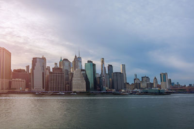 Modern buildings by river against sky in city