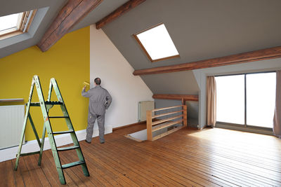 Painter painting a yellow wall in a renovated interior attic.