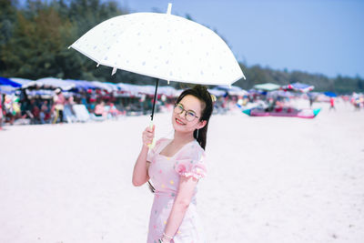 Portrait of smiling woman holding umbrella standing on beach against sky
