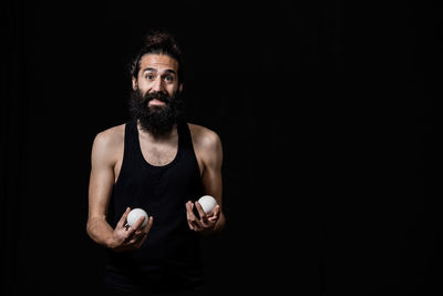 Portrait of bearded man with balls while standing against black background