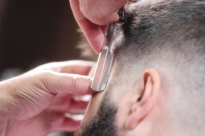 Cropped hands of barber cutting male customer hair with razor in salon