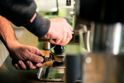 Cropped hands of man holding portafilter by espresso maker