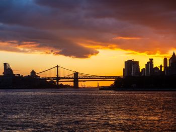 Silhouette bridge over river against sky during sunset