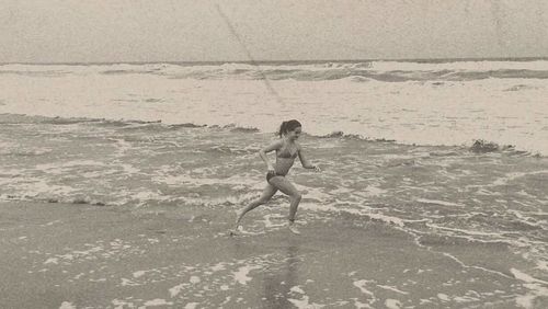 Full length of shirtless young woman standing on beach