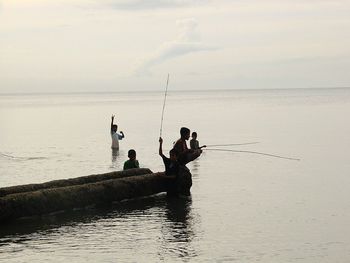 Boys fishing at river against sky