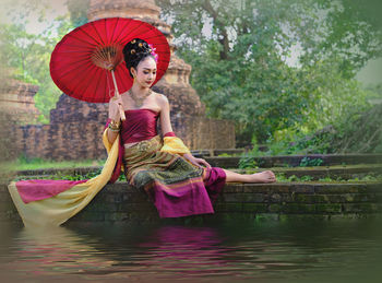 Full length of young woman wearing traditional clothing while sitting at lakeshore