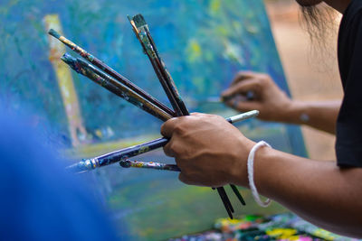 Cropped hand of painter holding paintbrushes while painting on canvas