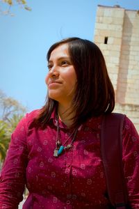 Young woman looking away while standing against clear sky