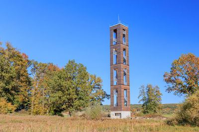 Tower amidst trees against clear blue sky