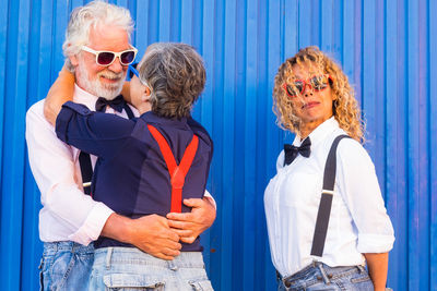 Woman standing by senior couple embracing against corrugated wall