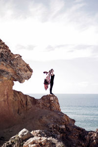 Woman standing on rock by sea against sky