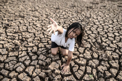 Portrait of girl gesturing while kneeling on cracked land