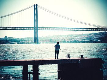 Man standing on bridge over river against sky