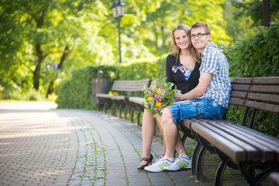 Portrait of couple with bouquet sitting on bench at park