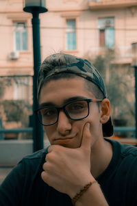 Close-up portrait of young man wearing eyeglasses against building