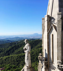 Statue by church against clear blue sky