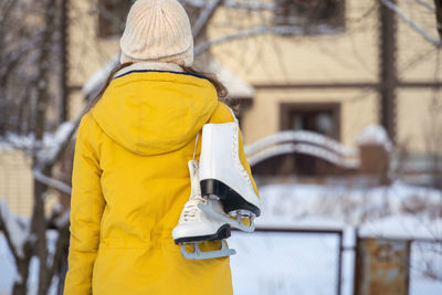 Young woman in yellow jacket with ice skates goes home.