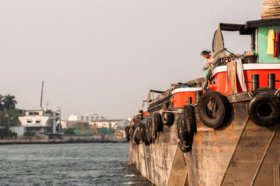 Woman sitting on ship in lake against clear sky