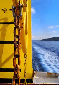 Close-up of rusty chain hanging by sea against sky