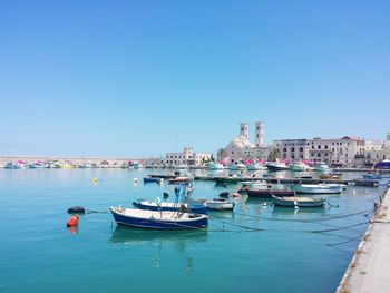 Boats moored in sea against clear blue sky