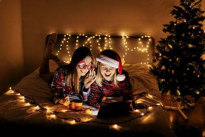 Two charming sisters lie on the bed with a laptop on christmas or new year's eve