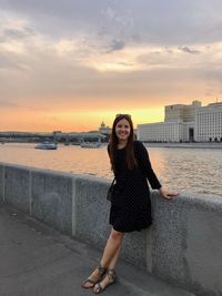 Portrait of smiling young woman standing against sea during sunset