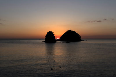 Silhouette rocks in sea against sky during sunset