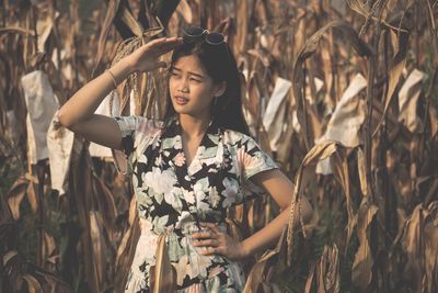 Fashionable young woman with hand on hip standing amidst plants on field