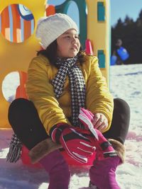 Cute girl sitting at snow covered playground