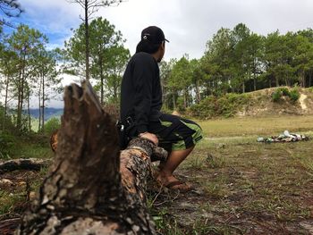 Man sitting on field against trees in forest