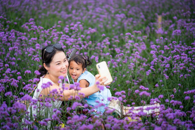 Smiling woman with daughter taking selfie amidst flowers on field 