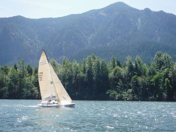 Sailboat sailing on sea against mountains