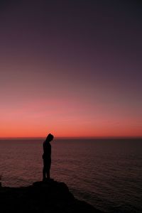 Side view of silhouette woman standing by sea against dramatic sky during sunset