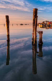 Reflection of wooden post in lake against sky during sunset