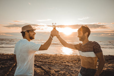 Friends standing on beach against sky during sunset