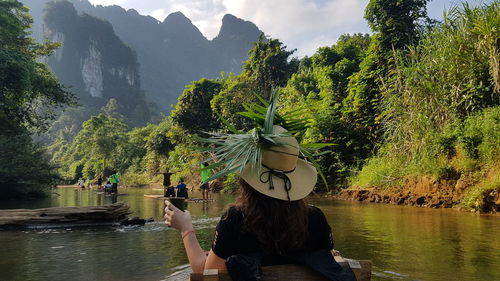 People by river against trees on mountain